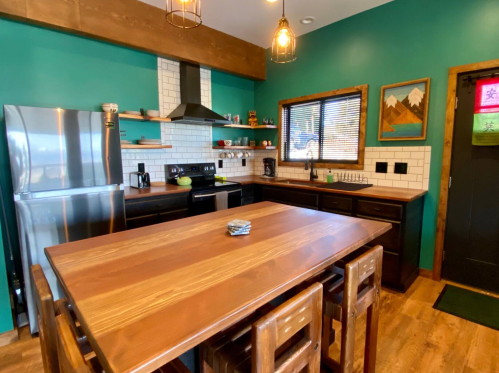 Modern kitchen with teal walls, wooden accents, stainless steel appliances, and a large wooden dining table.