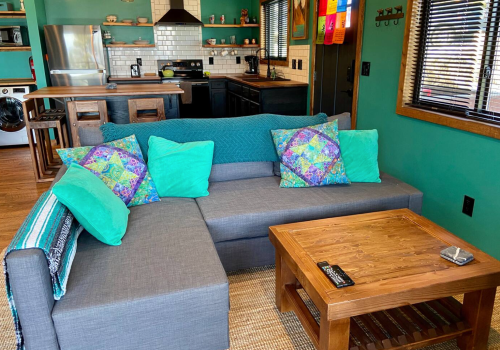 Cozy living area with a gray sectional sofa, colorful pillows, a wooden coffee table, and a vibrant teal wall.