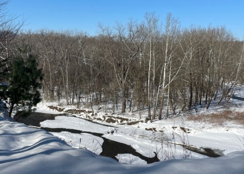 A snowy landscape with a winding river and bare trees under a clear blue sky.