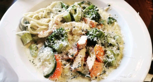 A plate of creamy pasta with chicken, broccoli, zucchini, and carrots, topped with grated cheese.