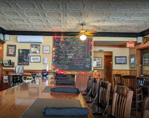 A cozy restaurant interior featuring a bar, wooden chairs, and a chalkboard menu with daily specials.