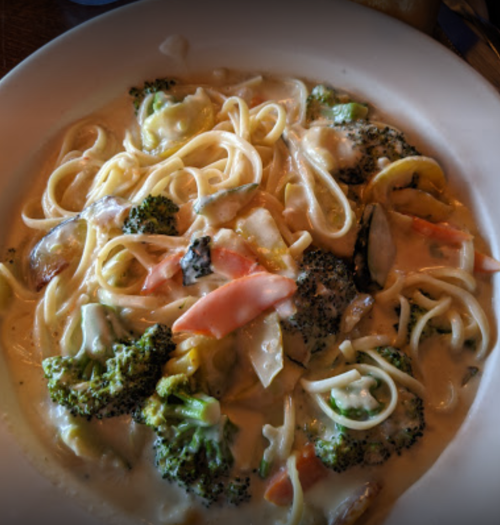 A plate of fettuccine pasta with broccoli, carrots, and a creamy sauce.