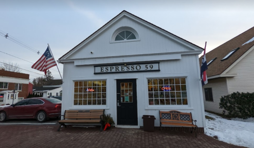 A white building with "Espresso 59" sign, featuring an American flag, benches, and snow on the ground.