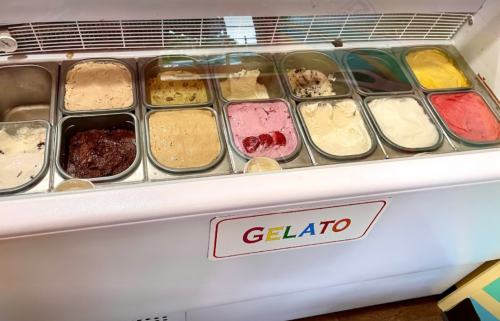 A display of various gelato flavors in metal containers, with a sign reading "GELATO" in front.