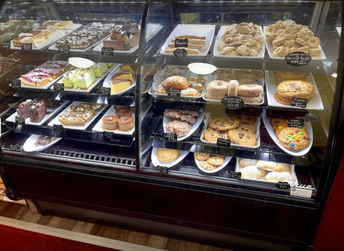 A display case filled with various baked goods, including cakes, cookies, and pastries, all labeled with names.