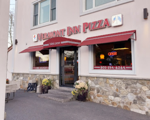 Exterior of Vermont Inn Pizza with a welcoming sign, open door, and flower pots on either side.