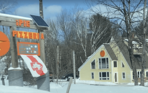 A snowy scene featuring a pizzeria sign and a yellow house with a large sun emblem.