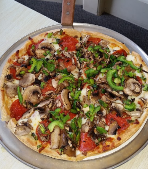 A freshly baked pizza topped with pepperoni, mushrooms, green peppers, and cheese on a round metal tray.