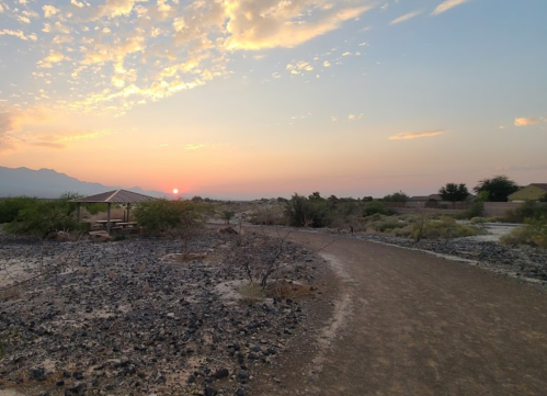 A serene landscape at sunset, featuring a path, rocky terrain, and a gazebo under a colorful sky.