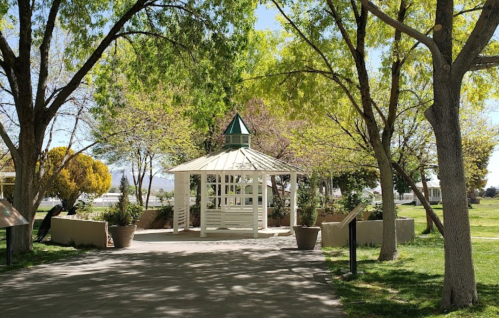 A peaceful park scene featuring a white gazebo surrounded by lush green trees and well-maintained landscaping.