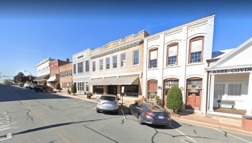 A quaint street view of a small town with historic buildings and parked cars under a clear blue sky.