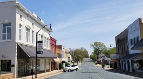 A quiet street scene in a small town, featuring shops and trees under a clear blue sky.