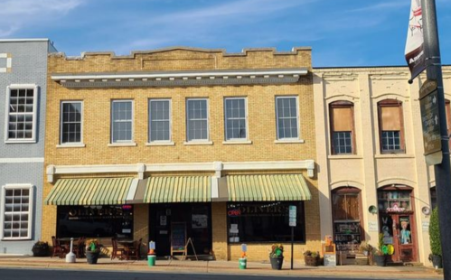 A charming brick building with large windows and striped awnings, featuring shops and outdoor seating.