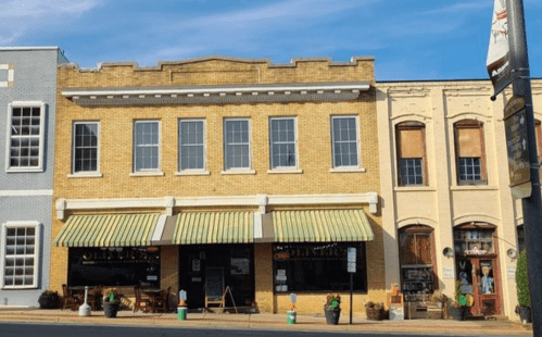 A charming brick building with large windows and striped awnings, featuring shops and outdoor seating.