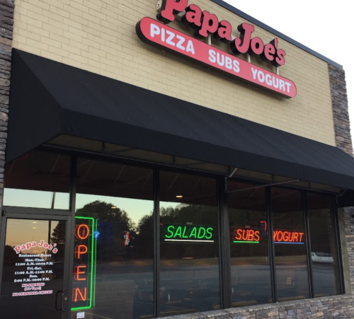 Exterior of Papa Joe's restaurant featuring neon signs for pizza, subs, yogurt, and salads, with an "Open" sign.