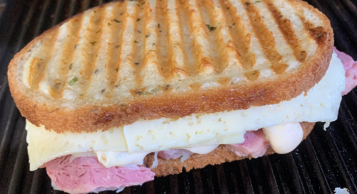 A grilled sandwich with layers of roast beef and melted cheese on toasted bread, showing grill marks on top.