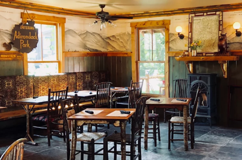 Cozy restaurant interior with wooden tables, chairs, and mountain-themed decor, featuring large windows and a fireplace.