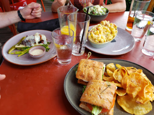A table with two sandwiches, chips, a salad, and drinks, including glasses of water and a cocktail.
