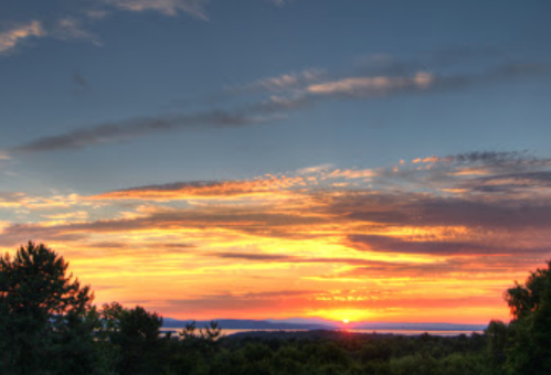 A vibrant sunset over a landscape, with colorful clouds and silhouettes of trees in the foreground.