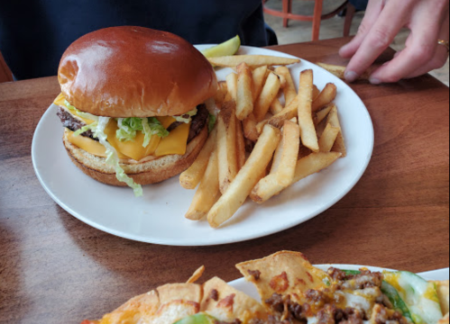 A plate with a cheeseburger topped with lettuce and fries on the side, set on a wooden table.