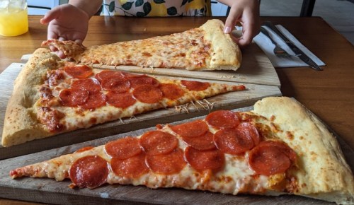 A person reaching for a slice of pepperoni pizza on a wooden board, with two large slices displayed.