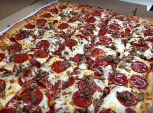 A large pizza topped with pepperoni and sausage, with melted cheese on a golden crust, in a pizza box.