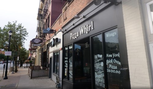 Exterior view of Pizza Whirl restaurant with large windows and signage, located on a city street.