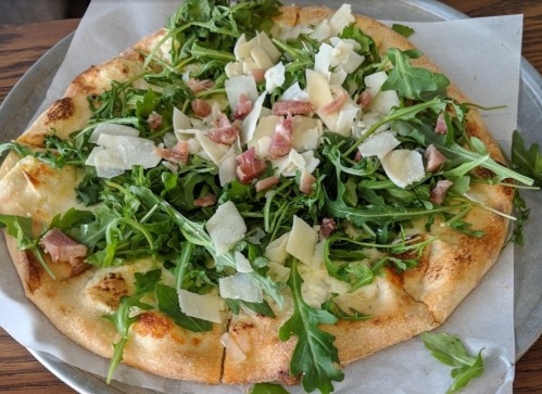 A pizza topped with fresh arugula, shaved Parmesan cheese, and bits of ham on a golden crust.