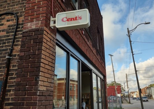 Sign for "Cents" on a brick building, with a clear sky and street view in the background.