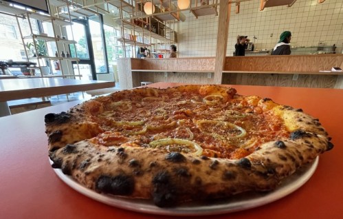 A close-up of a freshly baked pizza with a thick crust, topped with sauce and green peppers, on a table in a modern restaurant.