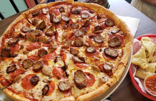 A large pizza topped with pepperoni and sausage, served with a side of breadsticks.