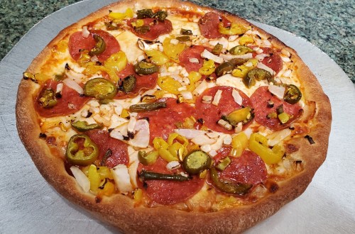 A freshly baked pizza topped with pepperoni, jalapeños, yellow peppers, and diced onions on a golden crust.