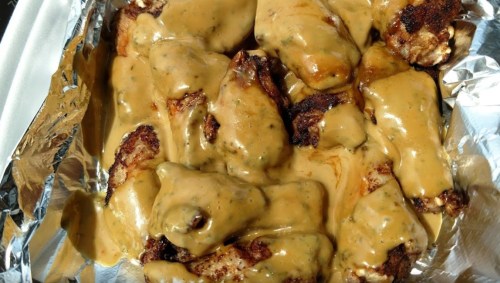 A tray of chicken wings covered in a creamy, golden sauce, resting on aluminum foil.