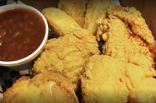 A box of crispy fried chicken pieces with a side of baked beans and a slice of cheesy bread.