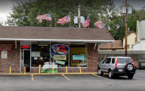 A small burger restaurant with an "Open" sign, flags on the roof, and a parked car outside.
