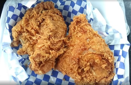 Two large pieces of crispy fried chicken on a blue and white checkered paper.