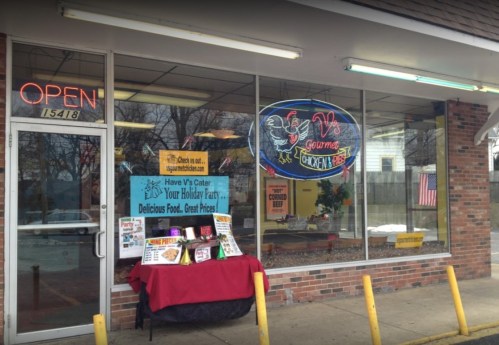 A storefront with a neon "Open" sign and a display table outside, featuring a menu and holiday catering information.