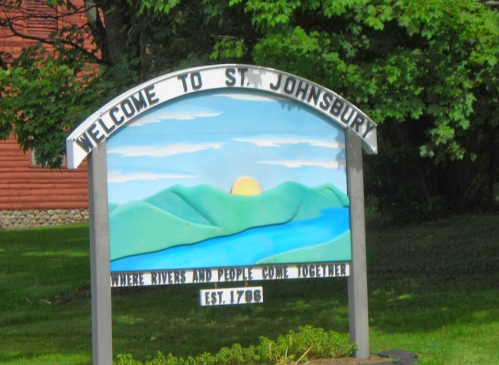 A colorful welcome sign for St. Johnsbury, featuring mountains, a river, and a sun, established in 1786.