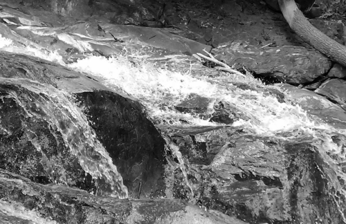 A close-up of flowing water cascading over rocky terrain in black and white.