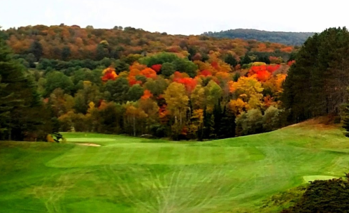 A scenic view of a golf course surrounded by vibrant autumn foliage in shades of red, orange, and yellow.