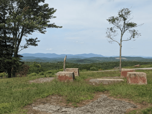 Scenic view of rolling mountains under a clear sky, with a tree and stone remnants in the foreground.