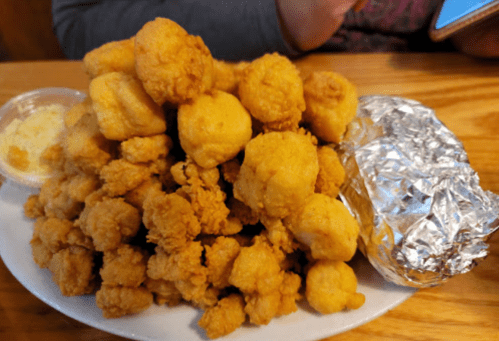 A large pile of golden fried food on a plate, with a side of butter and a foil-wrapped item.
