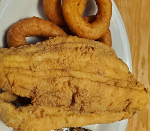 A plate featuring a large piece of fried fish alongside several golden onion rings.