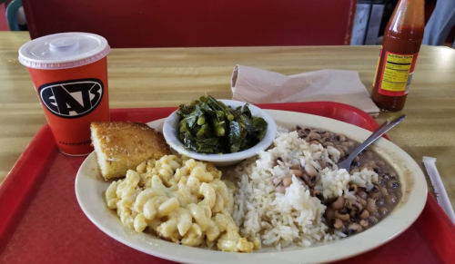 A plate of macaroni and cheese, rice, black-eyed peas, collard greens, cornbread, and a drink on a red tray.