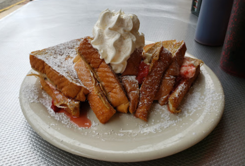 A plate of French toast topped with whipped cream and powdered sugar, with strawberry filling peeking out.