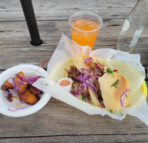 A plate with pulled meat sandwiches, purple cabbage, and a side of plantains, accompanied by a colorful drink.