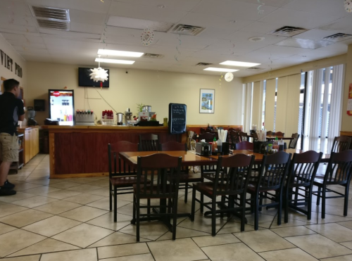 Interior of a casual restaurant with empty tables, a counter, and a man standing near the drink station.