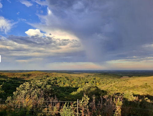 A scenic landscape with rolling hills, lush greenery, and a dramatic sky with clouds and a distant rain shower.