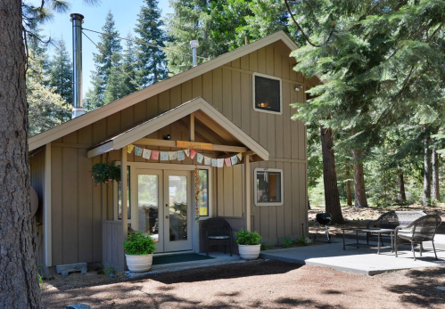 A cozy cabin surrounded by tall trees, featuring a welcoming entrance and outdoor seating area.