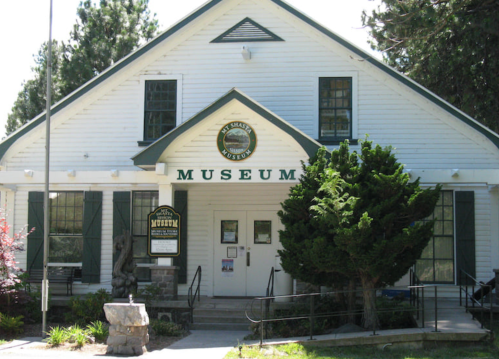 A white building with a sign reading "Museum," surrounded by trees and a stone pathway.